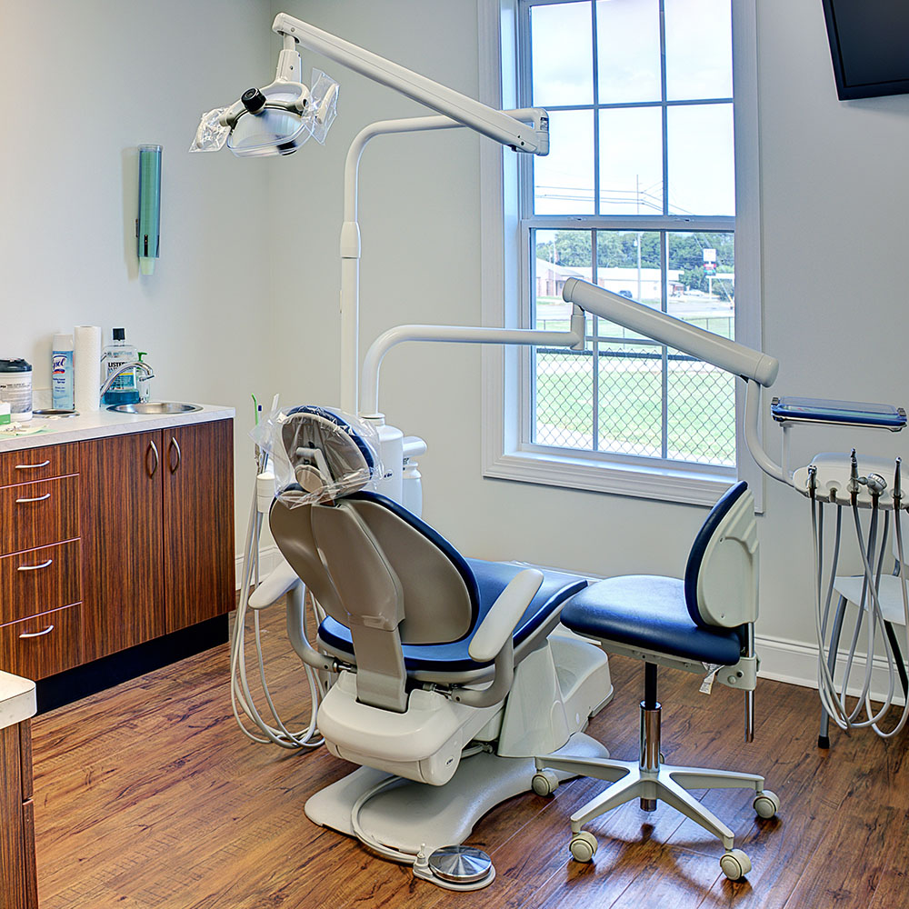 The image shows a dental office interior with a dental chair, a dental light, and various dental equipment.